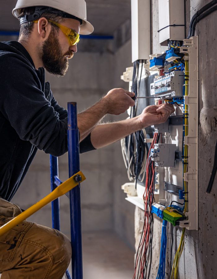 A male electrician works in a switchboard with an electrical connecting cable.