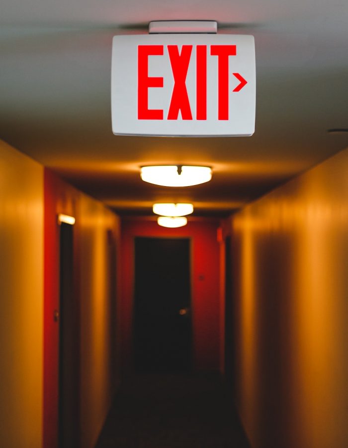 Exit sign in a lit up long hallway, exit to right from eerie hallway